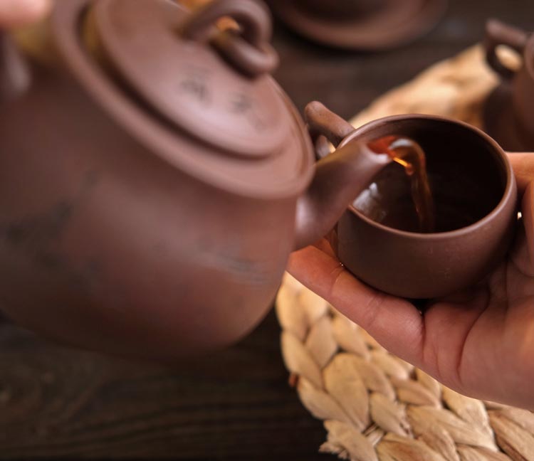 Ceramic teapot pouring tea into a matching cup held by a hand.