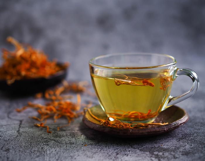 Clear glass cup of yellow tea with dried cordyceps mushrroms on a dark surface