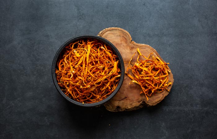 Dried cordyceps mushrroms in a black bowl and on a wooden surface against a dark background