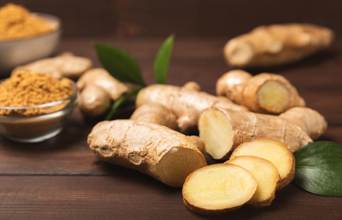 Fresh ginger roots and ground ginger powder on a wooden surface