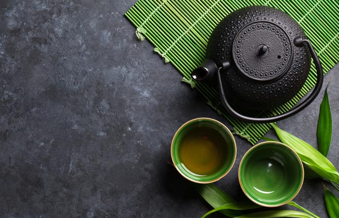 Black teapot and green tea cups on a dark surface with a green mat