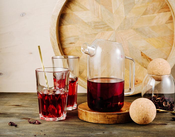 Clear glass pitcher and cups with Hibiscus  tea on a wooden surface.