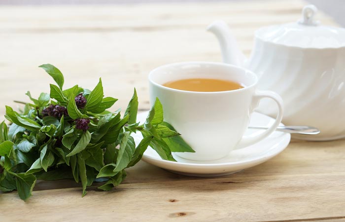 White cup of tea with teapot and fresh holy basil leaves on a wooden surface