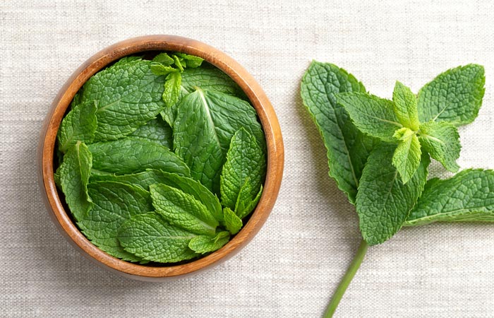 Wooden bowl filled with fresh green mint leaves on a light fabric background