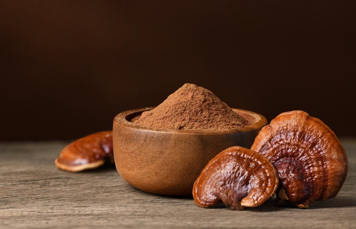 Wooden bowl with reishi powder and dried reishi mushrooms on a wooden surface