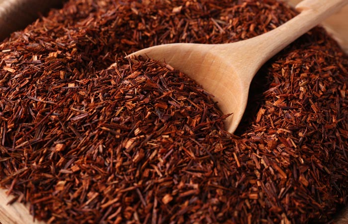 Close-up of dried red rooibos tea leaves with a wooden spoon.