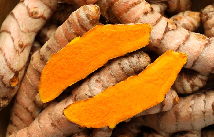 Turmeric root with bright orange slices on a background of whole turmeric roots.